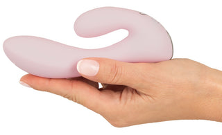 En hand håller CERYA Rabbitvibrator, en ljusrosa böjd minivibrator avsedd för vaginal och klitoral stimulering, mot en vit bakgrund.