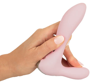 En hand som håller i CERYA Rabbitvibrator - en rosa, böjd minivibrator - mot en vit bakgrund, utformad för vaginal och klitoral stimulering.