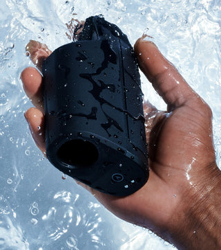 En hand håller Arcwave Ion 2 Masturbator, en svart vattentät enhet för män med innovativ Pleasure Air-teknik, under stänkande vatten.