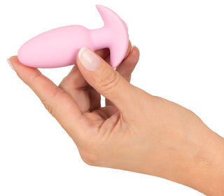 En hand håller i Cuties Mini Vibrating Plug, en liten rosa leksak som är idealisk för analplugg nybörjare som vill ha mjuka vibrationer, mot en vit bakgrund.
