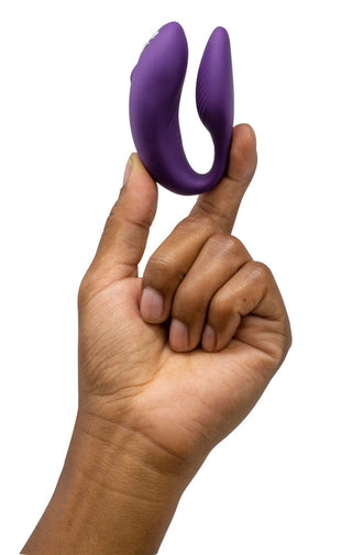 En hand håller i We-Vibe Chorus Parvibrator, en liten lila leksak, mot en vit bakgrund.