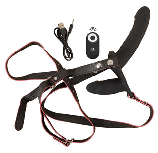 Svart vibrerande strap-on i silikon med dubbla remmar, fjärrkontroll och USB-kabel, avbildad mot en enfärgad vit bakgrund.