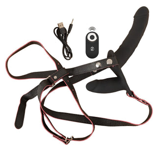 Svart vibrerande strap-on i silikon med dubbla remmar, fjärrkontroll och USB-kabel, avbildad mot en enfärgad vit bakgrund.