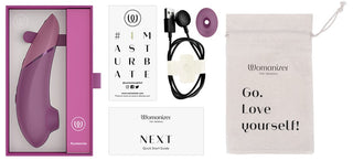 Womanizer NEXT Sensual Collection-stimulator i lila silikon med rundad spets och knappkontroller, visas med laddningskabel.