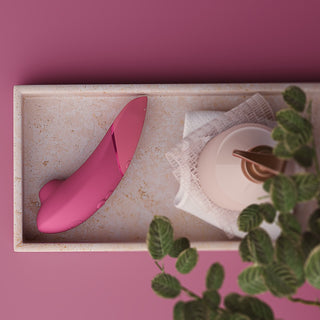 Rosa Womanizer NEXT Sensual Collection-apparat med slät yta, visas på en stenbricka.
