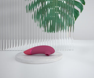 Pink Womanizer NEXT Sensual Collection, tillverkad av slätt material, vilar på en marmoryta.