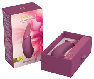 Womanizer NEXT-stimulator i rosa silikon i en öppen låda med slät, ergonomisk design. Blommig förpackning synlig i närheten.