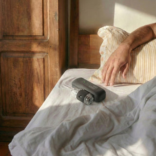 Masturbatorn Handy 2, en elegant svart enhet med en slät plastyta, placerad bredvid en CPAP-apparat i ett solbelyst sovrum.
