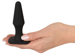 En hand håller i Magic Shiver Buttplug, en svart silikonplugg för nybörjare, mot en enkel vit bakgrund.