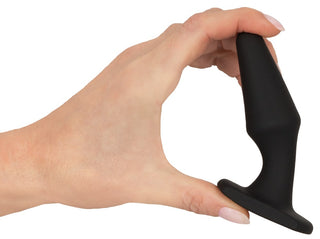 En hand håller Magic Shiver Buttplug, en liten svart analplugg i silikon perfekt för nybörjare, mot en vit bakgrund.