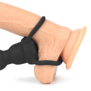 En hand håller i Lovetoy Dubbel Trouble Penisring, en svart gummiring för intimt bruk.