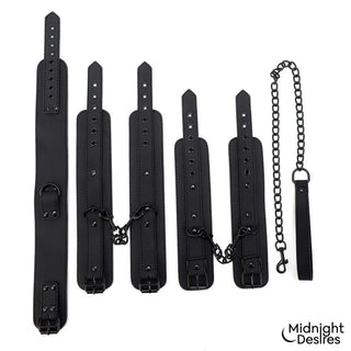 Ett bondage-set i svart veganskt läder med handbojor, halsband och kopplingskedjor, avbildat mot en vit bakgrund.