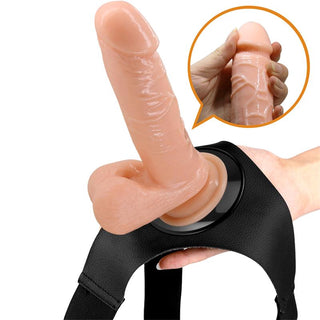 Realistisk dildo i hudfärgat silikon med sugpropp, fäst på en svart justerbar sele.