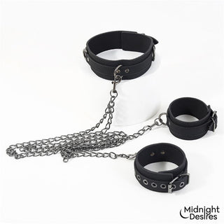 Svart halsband och fotbojor i veganskt läder, sammanlänkade med kedjor, med diskret logotyp.