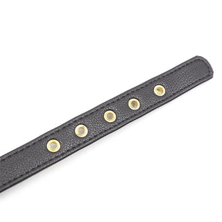 Närbilden visar Halsband Med Rosett, som visar upp ett svart läderband med sex guldöglor i rad, som frammanar en förförisk atmosfär.