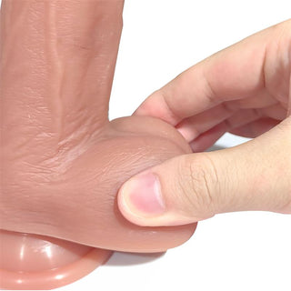 En hand som klämmer Realistisk Turbo Dildo med Rörelse, en realistisk mänsklig anatomimodell gjord av högkvalitativt flytande silikon, på en plan yta.