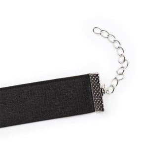 BDSM-halsbandet med svart rosett har ett justerbart band i svart sammet, silverspänne, förlängningskedja och en elegant svart rosett, mot en vit bakgrund.