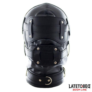 Total Lockdown BDSM Mask är en svart lädermask med remmar, metallnitar och en fäst krage för sensorisk begränsning; Latetobeg BDSM Line-logotypen finns i hörnet.