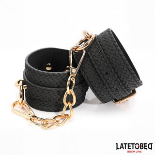Två svarta, texturerade Handbojor Med Guldfärgad Kedja fungerar som slående BDSM handledsfästen, sammanlänkade av en guldfärgad kedja och spännen. Perfekt som en snygg bondageaccessoar till din samling.