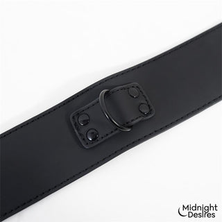 Svart rem i veganskt läder med D-ring i metall, ingår i Midnight Desires Bondageset Koppel, avbildad mot vit bakgrund.