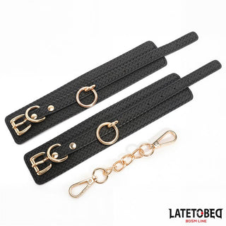 Handbojor Med Guldfärgad Kedja-svarta, texturerade handbojor med guldfärgade spännen och en avtagbar guldkedja, en elegant bondageaccessoar från Latetobeg BDSM Line.