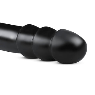 BUTTR MadBull Muzzl XXL Dildo är en svart segmenterad cylindrisk design med en lökformad ände, gjord av kroppssäkert material och visas mot en vit bakgrund.