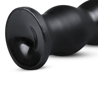 Närbild av ett svart cylindriskt föremål med en glänsande, rundad bas på en vit bakgrund, som påminner om den eleganta designen som finns i XXL Ribbad Buttplug från BUTTR.