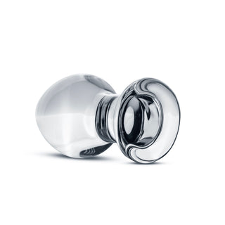 En genomskinlig, intrikat designad glasvikt med mjuka kurvor som påminner om en Glasklar Buttplug No. 26 ligger konstfullt på sidan mot en orörd vit bakgrund.
