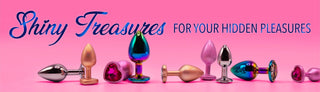 Flera metalliska buttplugs i olika färger och former, inklusive en med hjärtformad kristall, med texten Shiny treasures for your hidden pleasures