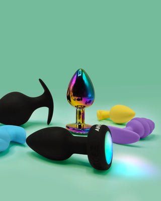 Regnbågsfärgad metallbuttplug tillsammans med silikonbuttplugs i olika färger på grön bakgrund.