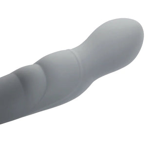 En roterande prostatastimulator, ljusgrå och slät, tillverkad av kroppssäker silikon, vilar på en vit bakgrund.