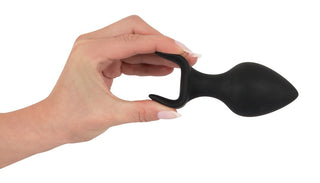En hand håller ett elegant svart Analplugg Trainer Set tillverkat av silikon, med en slät, avsmalnande ände, mot en orörd vit bakgrund.