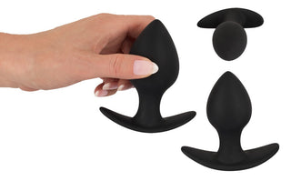 En hand håller försiktigt ett elegant svart Analplugg Trainer Set tillverkat av silikonmaterial, mot en orörd vit bakgrund.