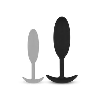 Buttplug Med Tyngd Medium"-setet innehåller två kroppsäkert silikonanalpluggar: en mindre grå och en större svart, båda med avsmalnande form och utsvängd bas, perfekt för vattenbaserat glidmedel.