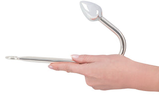 En hand håller den 24 cm Metall Analkrok, en elegant krok i rostfritt stål som är idealisk för bondageentusiaster. Med en ögla i ena änden och en tårformad spets på den andra, blandar den sömlöst elegans med funktion.