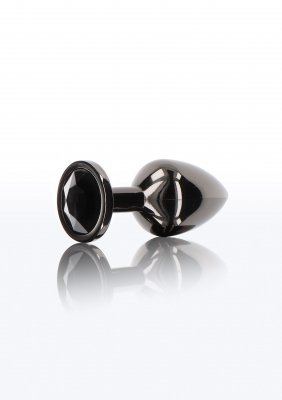 TabooM Analplugg Diamant Medium, en liten svart metallisk buttplug med ett facetterat ädelstensliknande handtag, skimrar på den vita ytan.
