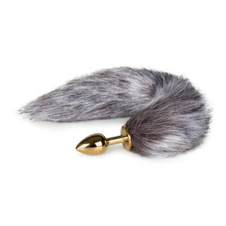 Produkten "Buttplugg med svans guld (liten)" är ett guldmetallföremål med en fluffig grå svans, perfekt för äventyrliga utforskningar.