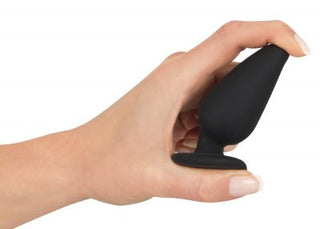 En hand håller i Analplugg medium silikon, en liten svart silikon butt plug med en utsvängd bas - en viktig sexleksak för dem som utforskar nya nöjen.