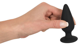 En hand håller elegant en medium Analplugg i elegant, svart silikon mot en orörd vit bakgrund.