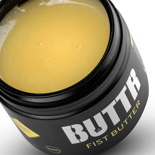 Den eleganta svarta burken med Buttr Fisting Butter innehåller en slät och krämig gul substans, perfekt för fisting äventyr.