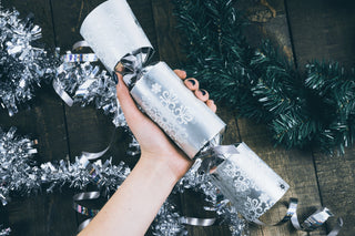 Hand som håller en silverfärgad julcracker bland juldekorationer – perfekt för julklappstips.