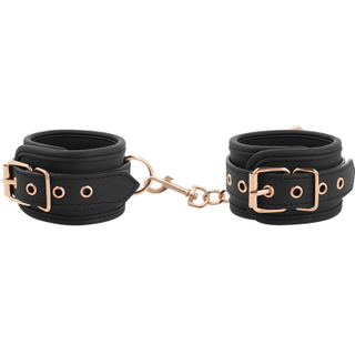 Coquette Fantasy Fotbojor är svarta läderhandbojor med eleganta roséguldspännen och en kopplingskedja, perfekt för att utforska bondage.
