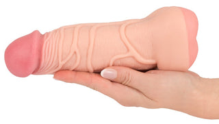 En person håller Penisförlängare / Vagina - 2 i 1, vilket framhäver det detaljerade hantverket hos denna premium sexleksak.