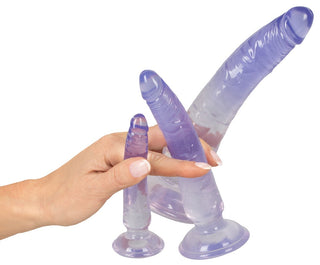 En hand håller You2Toys Crystal Clear Dildo Set, med tre lila dildos i olika storlekar, var och en med en sugkoppsbas för handsfree-nöje.