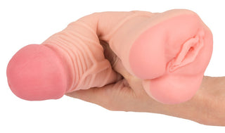 En hand som håller i en realistisk köttfärgad nyhet från produktlinjen "Penisförlängare / Vagina - 2 i 1" som liknar manliga könsorgan.