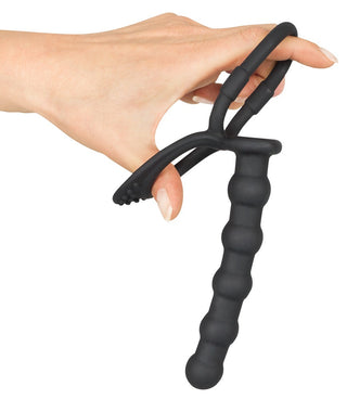 En hand håller ett texturerat svart föremål med ett ögla handtag och en räfflad bas – perfekt för dem som letar efter Double Trouble - Dubbel Penisring 13,5 cm-upplevelse.