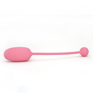 Magic Motion Kegeltränare Rosa, ett rosa trådlöst fjärrstyrt ägg designat för kegelövningar, har en lång anslutningssladd och kompatibilitet med Magic Kegel-appen, allt visas mot en orörd vit bakgrund.