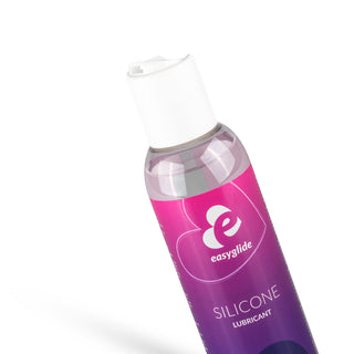 En lutad flaska Easyglide Silikonsmörjmedel med en lila och rosa gradientetikett visar en vit logotyp och text. Den har en CE-märkt etikett, en vit keps, vilar på en vanlig vit bakgrund och ger långvarig effekt.