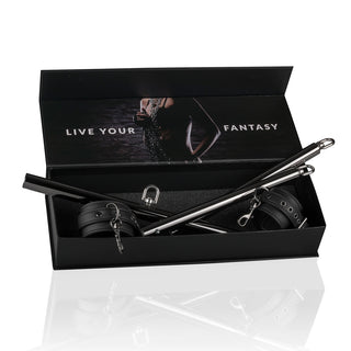 Öppen svart låda som innehåller BDSM-skydd och tillbehör, inklusive EasyToys Fotbojor/Handbojor Justerbar-spridare. Insidan av locket har "Live Your Fantasy"-text och en kroppssiluett.