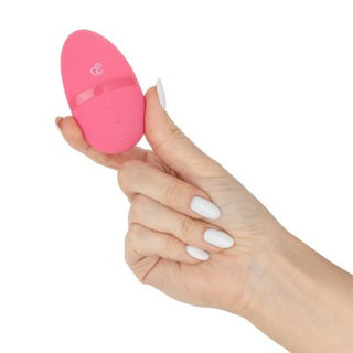 En hand med vitt nagellack håller den rosa Lay-on Vibrator - Rosa, formad som ett ägg med en subtil logotyp. Denna uppladdningsbar vibrator har en mjuk struktur och ett glänsande band runt dess mittparti, designat för ultimata klitorisstimulans.
